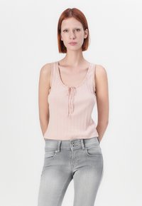 Lys rosa ribbestrikket tank topp med bølgede kanter og en sentral knute, kombinert med lys grå tettsittende jeans.