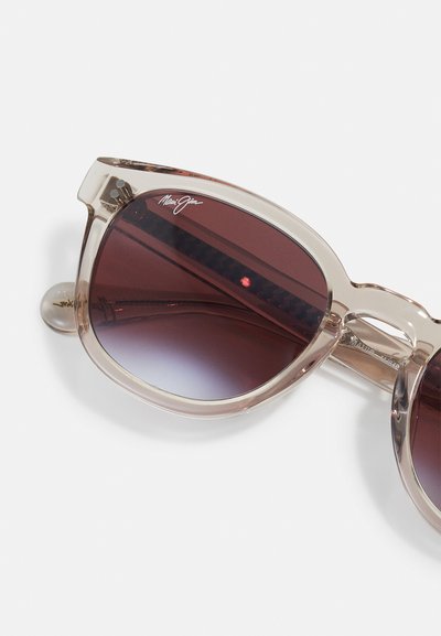 Sunglasses with a transparent beige frame, gradient dark red lenses, and a logo on the upper left lens. Features round temple tips.