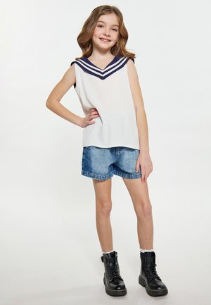 Hvid ærmeløs top med marineblå striber ved halsudskæringen, parret med lyseblå denimshorts og sorte snørrede støvler. Flad baggrund.
