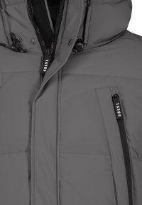 Graue Isolierjacke mit hohem Kragen, verstellbaren Kordeln, Reißverschlusstasche und dezentem Branding an Reißverschlüssen und Stoff.