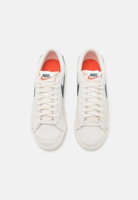 Paire de baskets blanches Nike avec logos swoosh noirs, lacets blancs et semelles intérieures rouges, vues de dessus sur fond blanc.