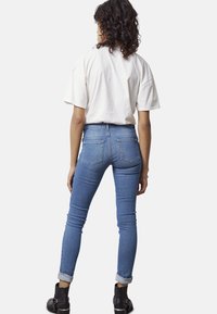 Vaqueros delgados de denim azul con una cintura alta, un lavado claro y dobladillos enrollados, combinados con una camiseta blanca holgada y botines negros.