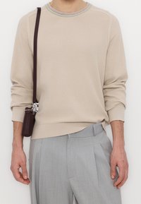 Beżowy dzianinowy sweter z fakturowanym wzorem, z wielokolorowym prążkowanym kołnierzem. Do tego jasnoszare, dopasowane spodnie i mała brązowa torebka.