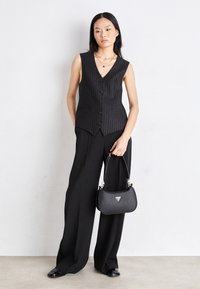 Sort stribet ærmeløs vest med fem knapper, kombineret med vide sorte bukser. Accessories inkluderer en lille sort håndtaske.