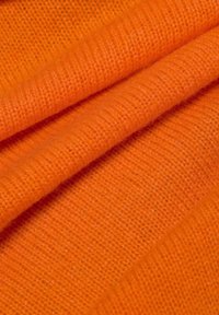 Oranje stof met een zachte, gestructureerde afwerking, met een gebreid patroon. De vezels zijn enigszins pluizig, wat een warme uitstraling creëert.