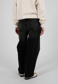 Jeans in denim nero dalla vestibilità ampia, con tasche posteriori. Abbinati a una felpa beige chiaro e scarpe bianco sporco.