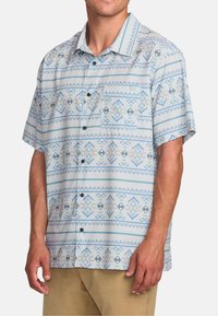 Kortærmet, button-up skjorte i lyseblå med geometrisk mønster. Har en lomme og kontrasterende mørke knapper. Fremstillet af åndbart stof.