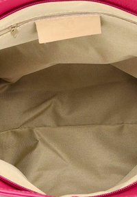 Roze handtas interieur met een gladde, beige stoffen voering met minimale textuur en een label nabij de bovennaad.