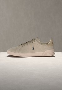 Μπεζ χαμηλό casual αθλητικό παπούτσι με σχεδιασμό με κορδόνια, λογότυπο Polo στο πλάι και στη φτέρνα και λαστιχένια σόλα, εμφανιζόμενο σε ουδέτερο φόντο.