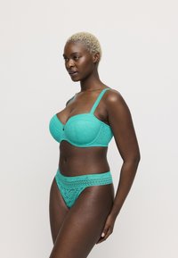 Turquoise kanten beha met beugel en verstelbare bandjes, gecombineerd met bijpassende kanten slip met gedetailleerde patronen en een decoratieve tailleband.