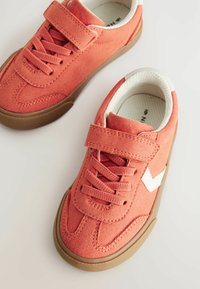 Różowe zamszowe sneakersy z białymi akcentami, z żakardowym zapięciem i rzepem. Gumowa podeszwa i teksturowana powierzchnia zapewniająca przyczepność.
