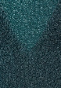 Turbankowy sweter z splotu w dekoltem w kształcie V. Tkanina ma subtelny połysk i teksturowany wzór, co podkreśla lekki, przewiewny splot.