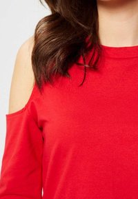 Top rojo sin mangas hecho de una tela suave y elástica; cuenta con mangas largas y una textura suave.