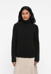 Temno rebrast pulover s turtleneck iz dolog rokavov. Narejen je iz teksturirane pletenine, ima sproščen kroj in visok ovratnik.