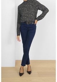 Granatowe obcisłe dżinsy w połączeniu z czarną koszulą w kwiatowy wzór z długim rękawem oraz czarne szpilki z zaostrzonym noskiem. Pasek z złotą klamrą.