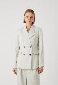 Světle barevný, dvojitý blazer s jemným proužkem a klopovým límcem, černými knoflíky a přizpůsobeným střihem, doplněný o odpovídající kalhoty.