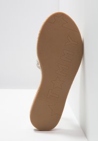 Podeszwa buta z teksturowanej, beżowej gumy, z wygrawerowanymi napisami "TOMMY" oraz wzorami gwiazdek. But ma zaokrąglone krawędzie.