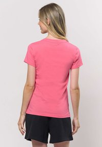 Tričko s krátkym rukávom z jasne ružovej látky, s okrúhlym výstrihom a priliehavým strihom, v kombinácii s tmavými šortkami. Minimalistický dizajn s hladkou textúrou.