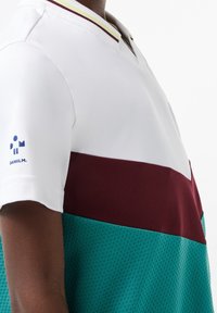 Koszulka polo z białym kołnierzykiem w żółte i burgundowe paski, bordową górną częścią oraz tealową dolną częścią o siateczkowej strukturze.