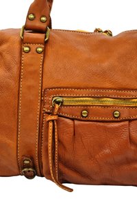 Sac en cuir marron avec une surface texturée, des accents en laiton, une poche zippée et des détails de couture contrastés.