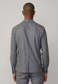 Camicia a righe grigie con maniche lunghe, polsini con bottone e un dettaglio sul retro. Realizzata in tessuto testurizzato con vestibilità sartoriale.