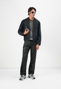 Melnas džinsa jaka ar rāvējslēdzēju, pelēks grafiskais T-krekls, melnas ādas bikses un pelēki sporta apavi ar daudzkrāsainiem akcentiem.