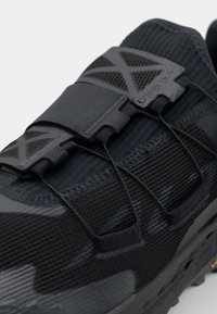 Black running shoe with a textured upper, elastic lacing system, and a reinforced toe section. Features a rugged sole for traction.