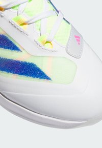 Chaussure de sport blanche avec un dessus texturé de couleur vert vif, complété par des accents bleus et roses, des éléments réfléchissants et un système de laçage.