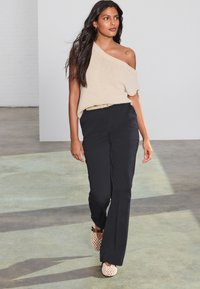 Šviesiai rudas pečius atidengiantis megztinis derinamas su juodomis platėjančiomis kelnėmis ir šviesaus atspalvio perforuotomis balerinomis. Paprasta diržas pabrėžia liemenį.