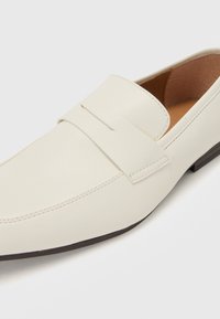 Valkoiset nahka loaferit, joissa on ommeltu muotoilu, etuolka ja matala ruskea pohja, sekä sileä pinta kauttaaltaan.