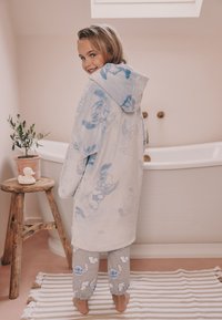 Peignoir en polaire bleu avec une capuche, orné d'un motif de personnage de dessin animé. Pantalon de pyjama gris avec des motifs de personnages bleus et des ourlets côtelés.