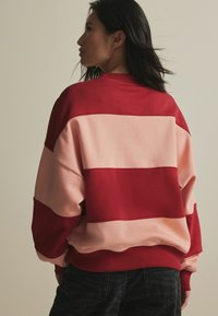 Värviline sweatshirth koos laiadest punastest ja roosadest triipudest. Valmistatud pehmest kangast, omades mugavat lõiget ning soonikku cuffs ja hem.
