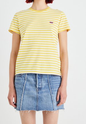Person iført gul og hvidstribet kortærmet skjorte med rød logo og blå denimnederdel med frynset kant og lodrette sømme.
