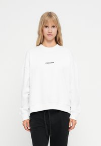 Biela mikina s cropped strihom, okrúhlym výstrihom a dlhými rukávmi. Vlastnosti zahŕňajú text "PEGADOR" v čiernej farbe nad hrudníkom.