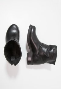 Botas de cuero negro hasta el tobillo con puntera redonda, tacón bajo y textura suave. Presentan acentos cosidos y un diseño sin cordones.