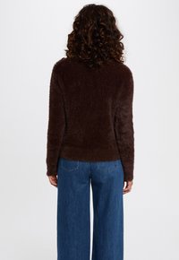 Maglione soffice di un marrone scuro con una texture morbida e orlo a coste, abbinato a jeans blu a gamba larga.