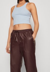 Haut court à rayures bleu clair avec des larges bretelles associé à un jogging en simili cuir bourgogne foncé avec une taille élastique et des poches latérales.