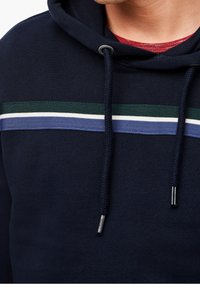 Felpa navy con cappuccio regolabile, caratterizzata da righe orizzontali verdi, bianche e blu sul petto. Tessuto morbido al tatto.