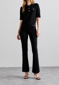 Czarna skórka polo z krótkimi rękawami i kołnierzykiem, z trzema guzikami i kieszeniami. Połączona z dopasowanymi czarnymi spodniami dzwonami i szpilkami.