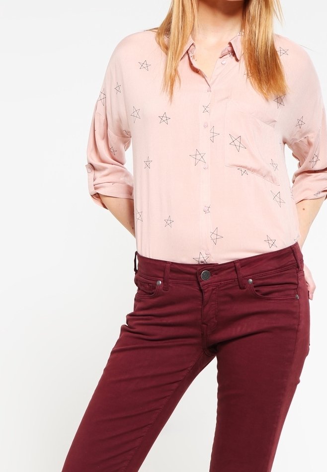 Chemise boutonner rose clair avec un motif d'étoiles et des manches retroussées, associée à un pantalon ajusté bordeaux. Tissu doux et coupe tailleur.
