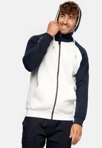 Sudadera con capucha que presenta un cuerpo blanco con mangas marinas, cierre de cremallera, cordones y un bolsillo tipo canguro. Material suave de mezcla de algodón.