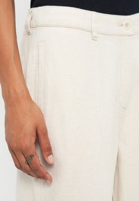 Pantalone od lana krem boje s ravnim krojem, s bočnim džepovima i zatvaranjem na gumb, teksturirana tkanina i minimalne šavove.