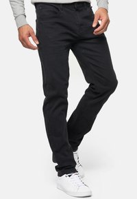 Vaqueros de mezclilla negra con corte ajustado, presentando una cinturilla estándar, diseño de cinco bolsillos y detalles de costura visibles. Combinados con zapatillas blancas.