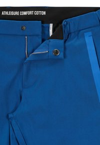 Blå träningsbyxor i bomull med svart midja, med dragkedja, knäppning och sidostripdetalj. Slät textur.