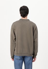 Oversized olive green sweater with a polo collar, ribbed cuffs, and hem, paired with light blue distressed jeans.