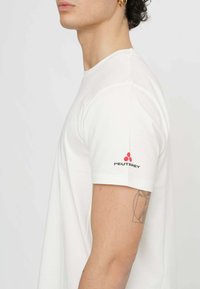 T-shirt blanc à col rond avec des manches courtes, une coupe décontractée, et un logo Peuterey noir et rouge sur la manche gauche. Texture de tissu lisse.