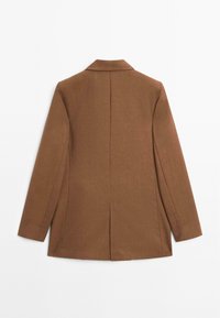 Veste marron sur mesure à manches longues, avec une couture centrale dans le dos et une petite fente arrière, présentée à plat de dos sur un fond blanc.