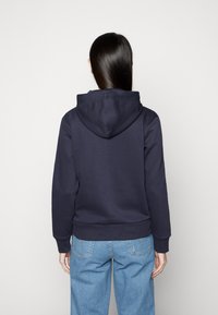 Tricou cu glugă de culoare bleumarin, cu o textură moale și manșete ribinate, asortat cu blugi din denim de culoare albastră deschisă. Spatele are un design lejer.