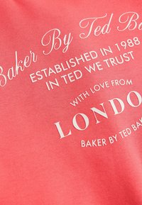 Korallikangas valge tekstiga. Tootemärgiks on "Baker By Ted Baker", asutamisaasta ja asukoht "London", ringikujuliste aktsentdetailidega.