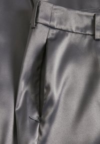 Gros plan sur un tissu en satin gris, confectionné avec une ceinture, une boucle de ceinture et une fermeture éclair latérale partiellement ouverte.